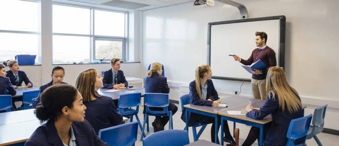 Teacher stood at the front of the classroom teaching a lesson to pupils