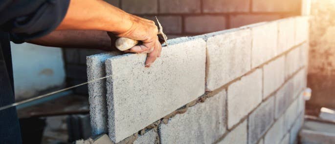 Person's hand laying grey bricks with mortar 