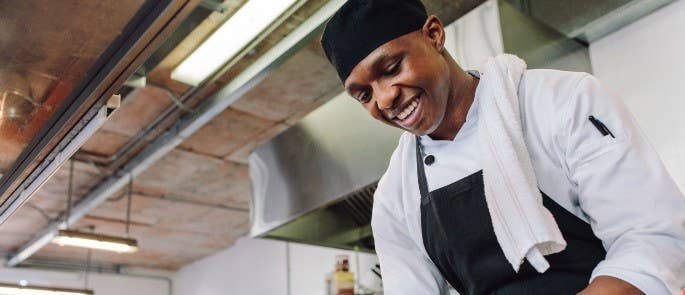 Chef working in a kitchen wearing a chef hat, jacket and apron