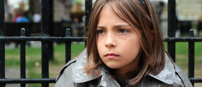 A young girl sits unsupervised outside school gates