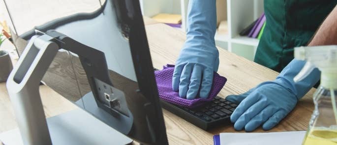 Cleaner wiping keyboard on office computer desk