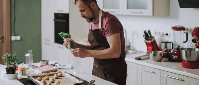 Man wearing an apron icing his cupcakes.