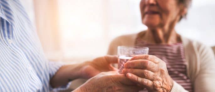 Healthcare professional ensuring an elderly person drinks enough water and making sure they aren't dehydrated