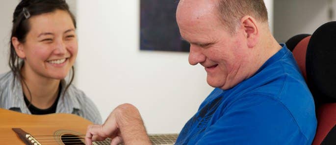 Adult with support needs playing guitar in front of his carer