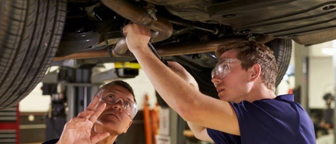 Young apprentice mechanic working under raised car