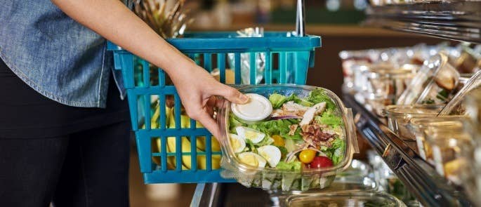 A customer selecting a pre-made salad and putting it into her basket