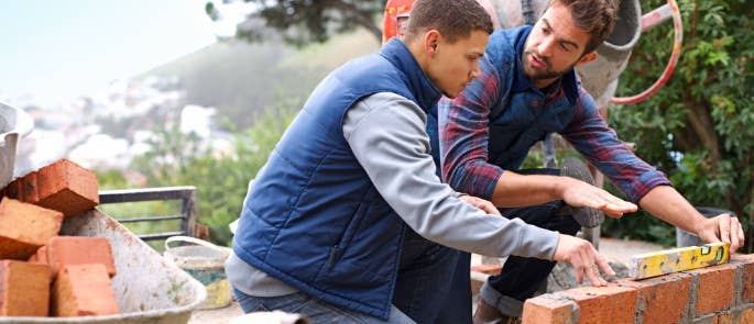 Worker and apprentice learning how to bricklay