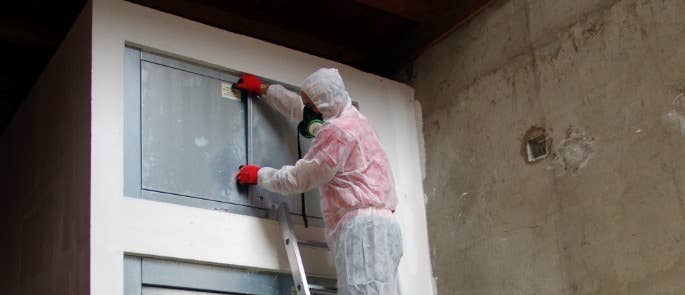 Worker on ladder in overalls and wearing respirator