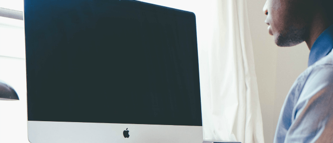 man sitting down to a mac computer